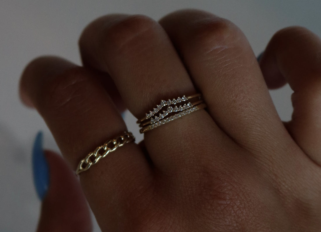 three dainty diamond ring bands stacked on each other and a chain ring on a hand