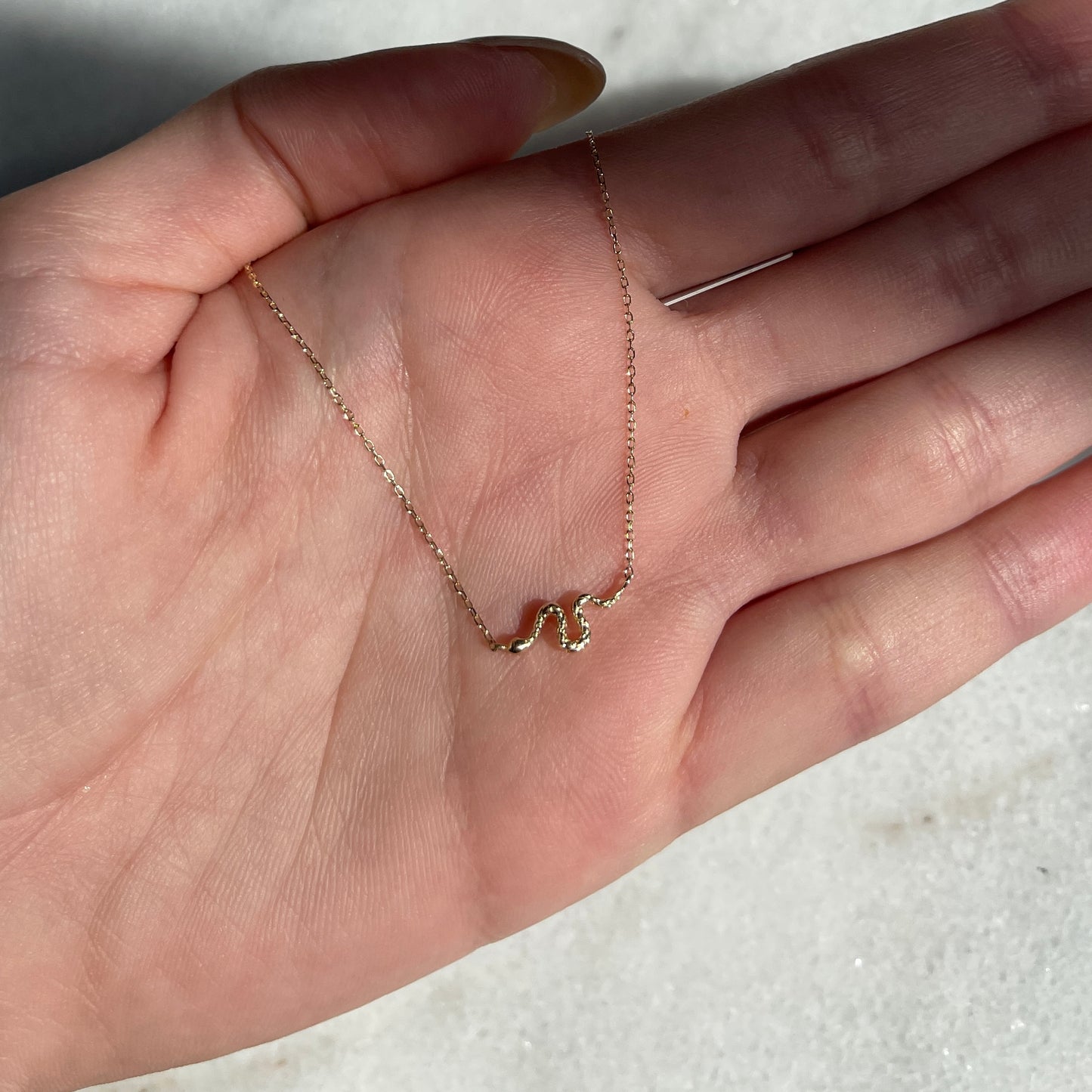 dainty 14k gold serpent necklace in palm of hand