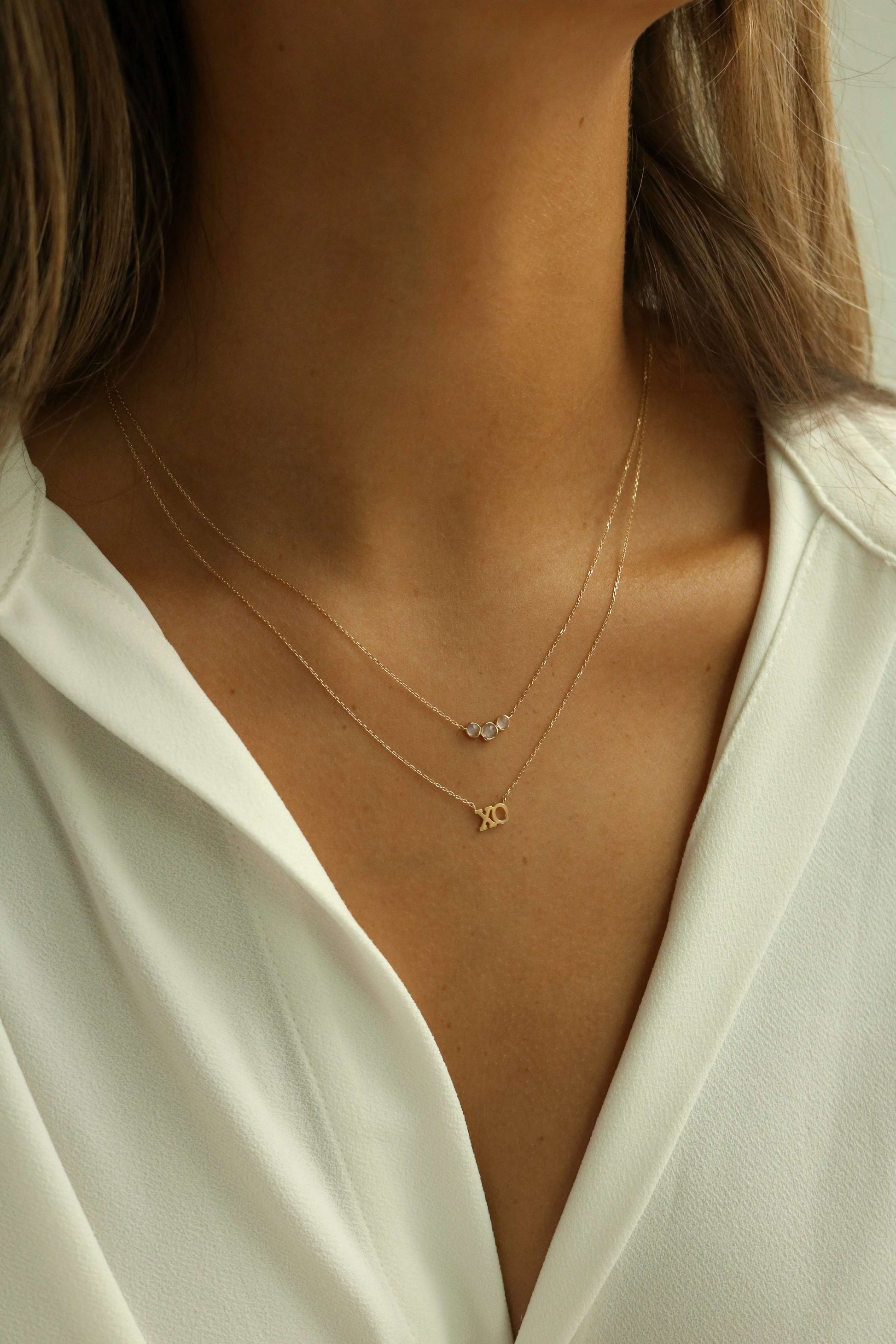 14k gold XO necklace layered with a triple moonstone pendant on tan skin collarbones
